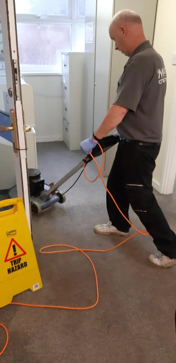 Millers cleaner operating a floor cleaning machine beside a wet floor sign